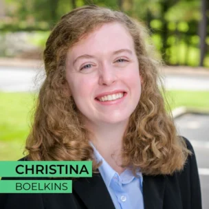 A young woman with curly hair smiles while standing outside on a sunny day. Text overlay says "Christina Boelkins".