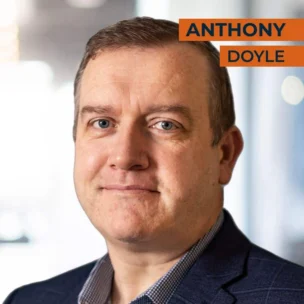 A man with short brown hair is wearing a blue suit and checkered shirt, with the name "Anthony Doyle" written in orange text on the top right of the image.